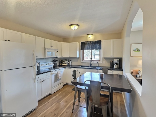 kitchen with dark countertops, light wood-style flooring, white cabinets, white appliances, and a sink