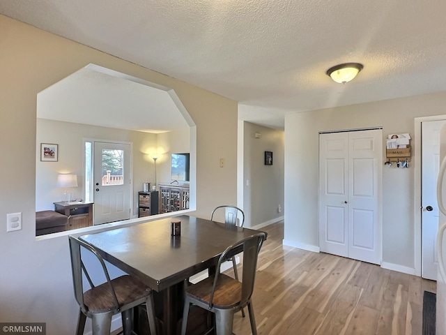 dining area featuring baseboards, arched walkways, light wood finished floors, and a textured ceiling