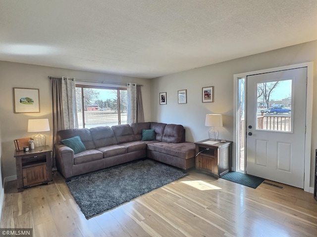 living area with visible vents, light wood-style floors, and a textured ceiling