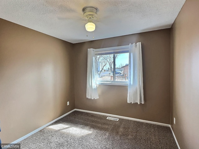 spare room featuring a textured ceiling, carpet, visible vents, and baseboards