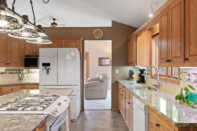 kitchen featuring vaulted ceiling, white appliances, a sink, and light stone counters