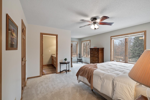 bedroom with a textured ceiling, light carpet, a ceiling fan, baseboards, and ensuite bath