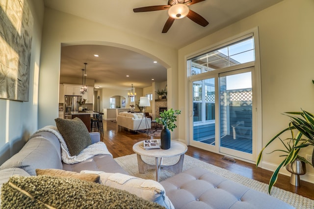 living room with ceiling fan with notable chandelier, plenty of natural light, and dark wood-type flooring