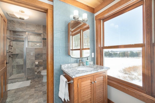 full bath with toilet, a wealth of natural light, tile walls, and vanity