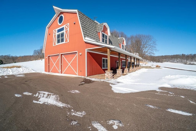 view of snowy exterior with an outbuilding, a detached garage, a barn, and a gambrel roof