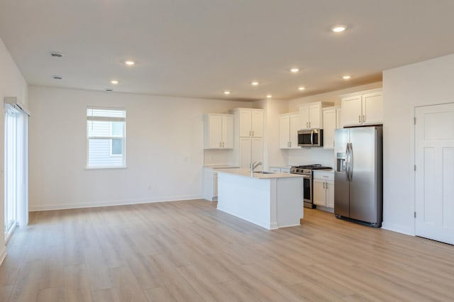 kitchen featuring light wood-type flooring, stainless steel appliances, an island with sink, sink, and white cabinetry