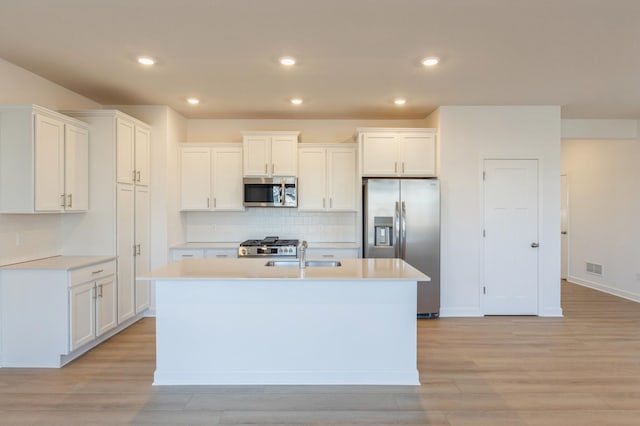 kitchen with a center island with sink, light wood-type flooring, stainless steel appliances, and white cabinetry