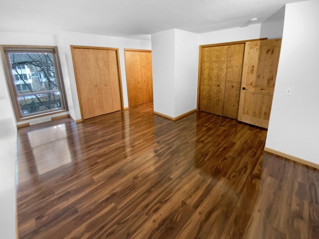 unfurnished bedroom featuring dark hardwood / wood-style flooring, a textured ceiling, and two closets