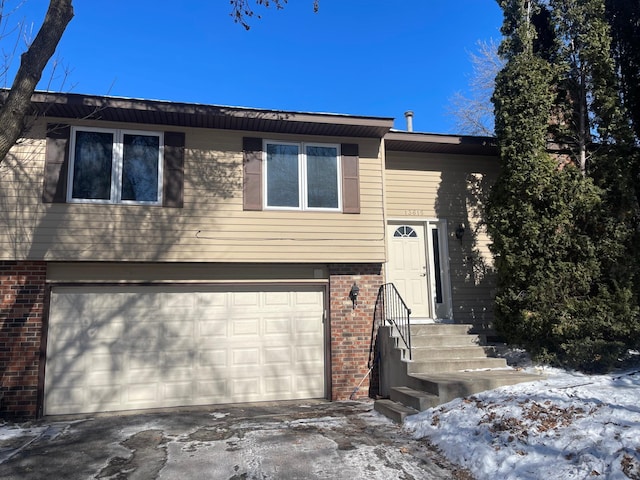 split foyer home with concrete driveway, brick siding, and an attached garage