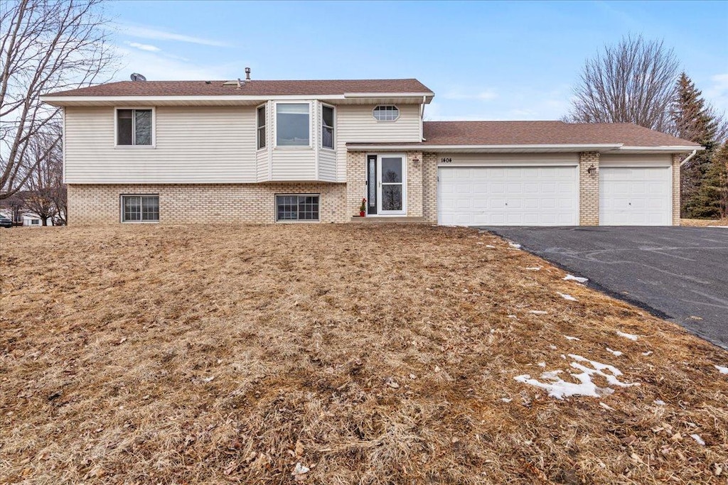 tri-level home with a garage, aphalt driveway, and brick siding