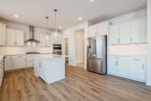 kitchen with hanging light fixtures, wall chimney exhaust hood, stainless steel appliances, a center island, and white cabinetry