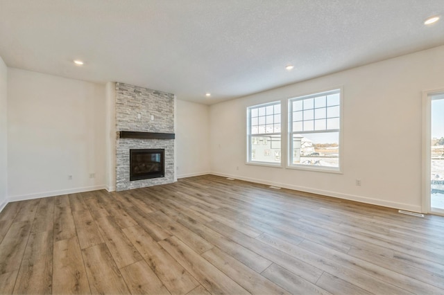 unfurnished living room with a stone fireplace, a textured ceiling, and light wood-type flooring