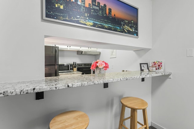 kitchen with white cabinets, appliances with stainless steel finishes, light stone counters, under cabinet range hood, and a kitchen bar