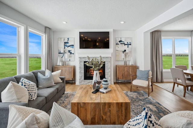 living room with a textured ceiling, a stone fireplace, and wood finished floors