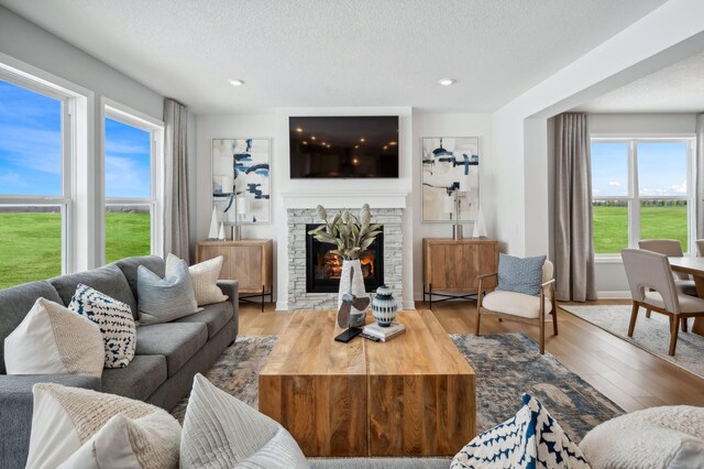 living room featuring recessed lighting, a stone fireplace, a textured ceiling, and wood finished floors