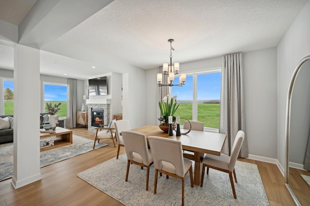 dining area with baseboards, an inviting chandelier, a textured ceiling, light wood-style floors, and a fireplace