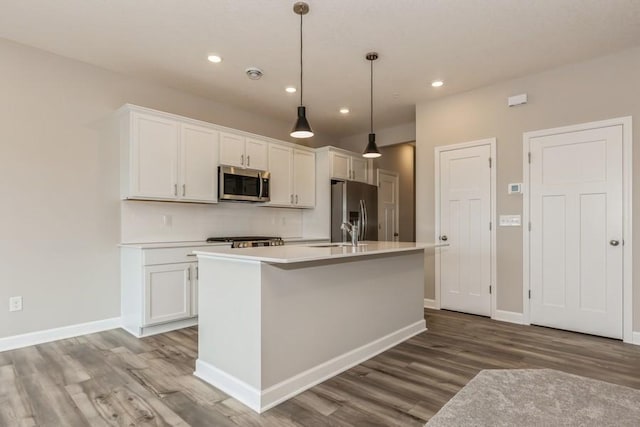 kitchen with a center island with sink, hardwood / wood-style flooring, appliances with stainless steel finishes, white cabinets, and pendant lighting