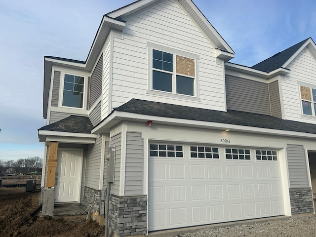 view of front of house featuring a garage, stone siding, central AC, and a shingled roof