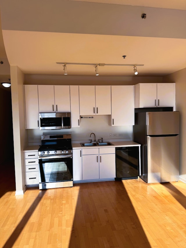 kitchen featuring white cabinetry, appliances with stainless steel finishes, light wood-style flooring, and a sink