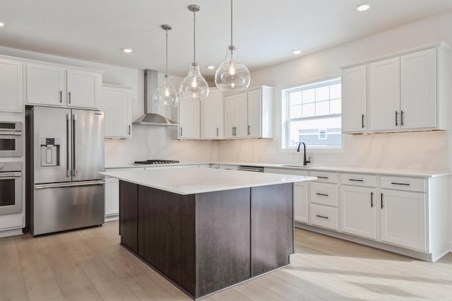 kitchen with white cabinetry, a kitchen island, stainless steel appliances, wall chimney exhaust hood, and hanging light fixtures