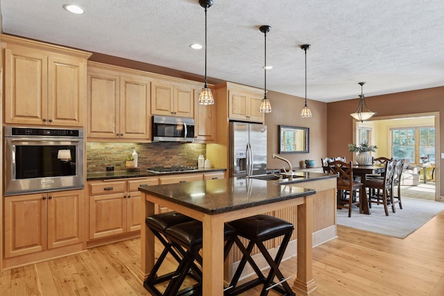 kitchen with sink, appliances with stainless steel finishes, a kitchen island with sink, and decorative light fixtures