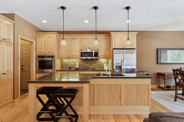 kitchen with a center island with sink, stainless steel appliances, pendant lighting, and light brown cabinets