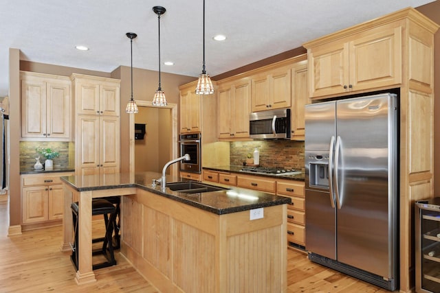 kitchen featuring an island with sink, sink, stainless steel appliances, and decorative light fixtures