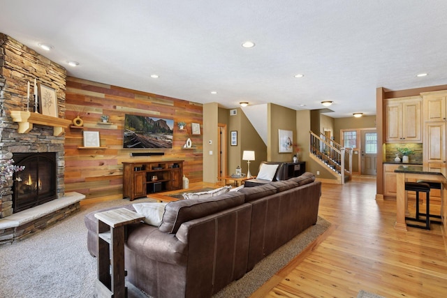 living room with a stone fireplace, wood walls, and light hardwood / wood-style floors