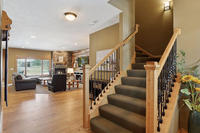 stairway with hardwood / wood-style flooring, a textured ceiling, and a fireplace