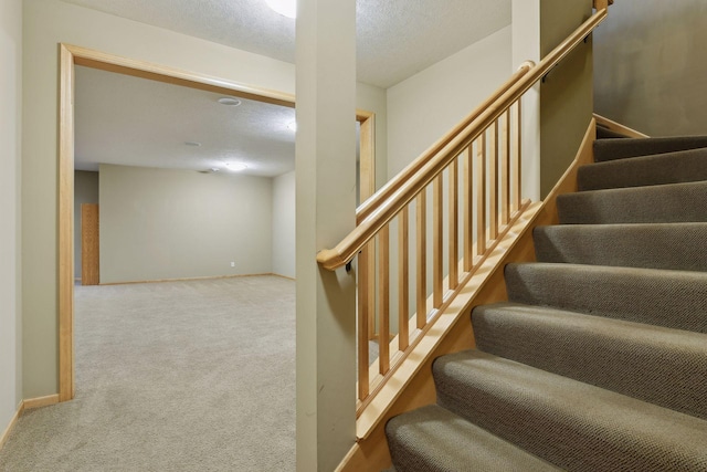 staircase featuring a textured ceiling and carpet flooring