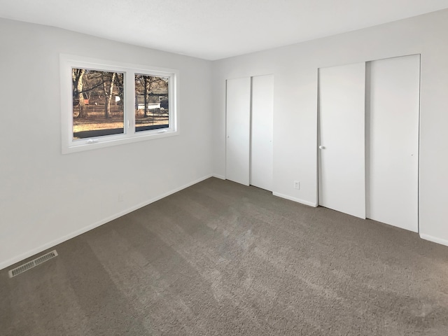 unfurnished bedroom featuring dark carpet and multiple closets