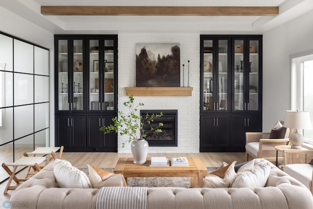 living room featuring a brick fireplace, light wood-type flooring, and beamed ceiling