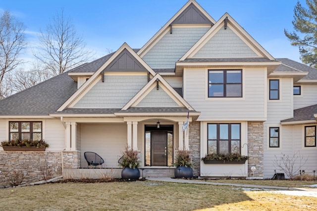 view of front facade featuring stone siding, a shingled roof, a front lawn, and board and batten siding