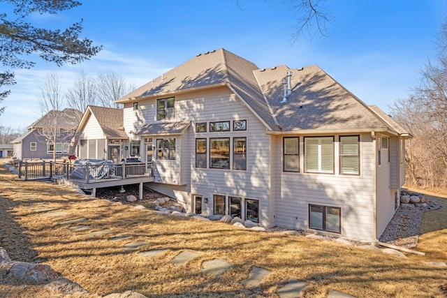 rear view of property featuring a deck, a lawn, and roof with shingles