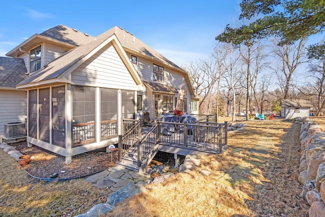 rear view of house featuring a deck, central AC unit, a shingled roof, an outdoor structure, and a sunroom