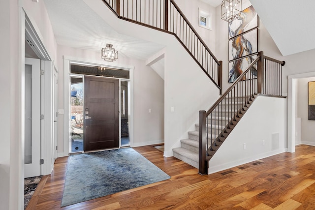 entryway with baseboards, wood finished floors, a towering ceiling, and a notable chandelier