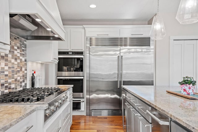 kitchen with decorative backsplash, light stone counters, custom exhaust hood, stainless steel appliances, and white cabinetry