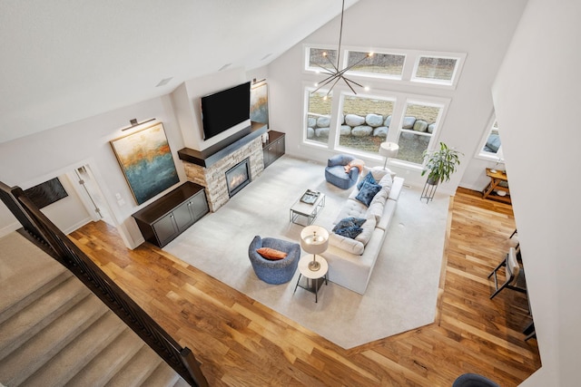 living area with a chandelier, high vaulted ceiling, a stone fireplace, wood finished floors, and stairs