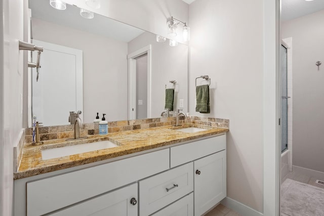 full bath featuring enclosed tub / shower combo, double vanity, a sink, and baseboards