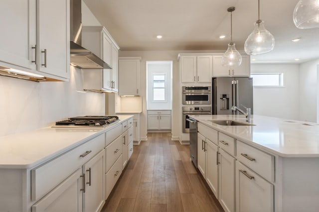 kitchen featuring white cabinetry, a kitchen island with sink, stainless steel appliances, sink, and wall chimney exhaust hood