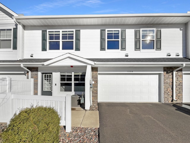 multi unit property featuring a shingled roof, stone siding, aphalt driveway, an attached garage, and fence