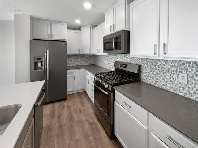 kitchen featuring sink, stainless steel appliances, dark wood-type flooring, white cabinets, and tasteful backsplash