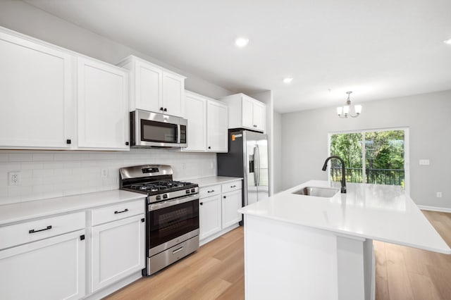 kitchen with a kitchen island with sink, stainless steel appliances, a sink, light wood-style floors, and decorative backsplash