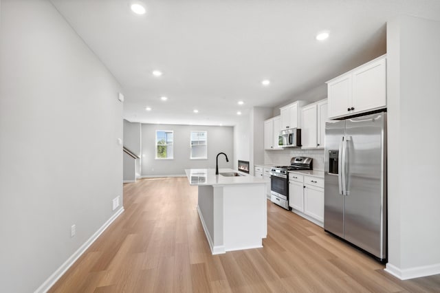 kitchen featuring stainless steel appliances, white cabinets, a sink, and light wood-style flooring