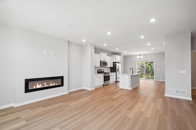 unfurnished living room with light wood-style floors, a glass covered fireplace, a sink, and recessed lighting