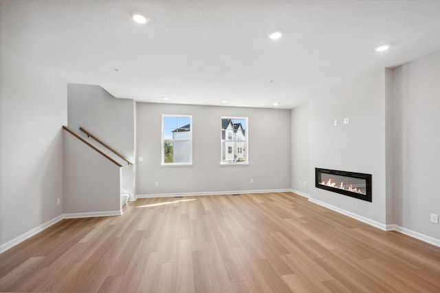 unfurnished living room featuring a glass covered fireplace, light wood-style flooring, baseboards, and recessed lighting