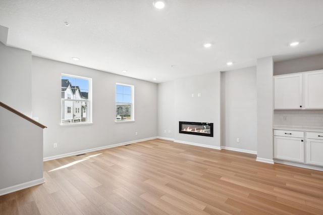 unfurnished living room featuring light wood-type flooring, recessed lighting, baseboards, and a glass covered fireplace