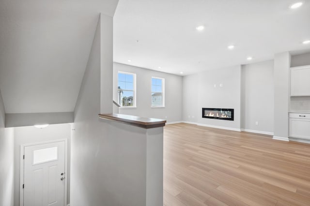 unfurnished living room featuring baseboards, recessed lighting, a glass covered fireplace, and light wood-style floors