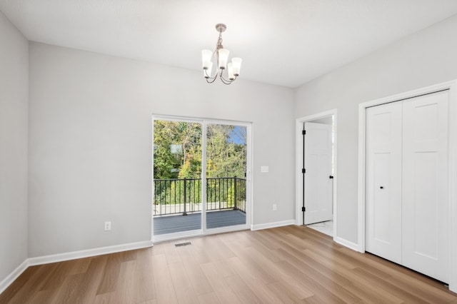 unfurnished bedroom featuring access to exterior, a notable chandelier, visible vents, wood finished floors, and baseboards