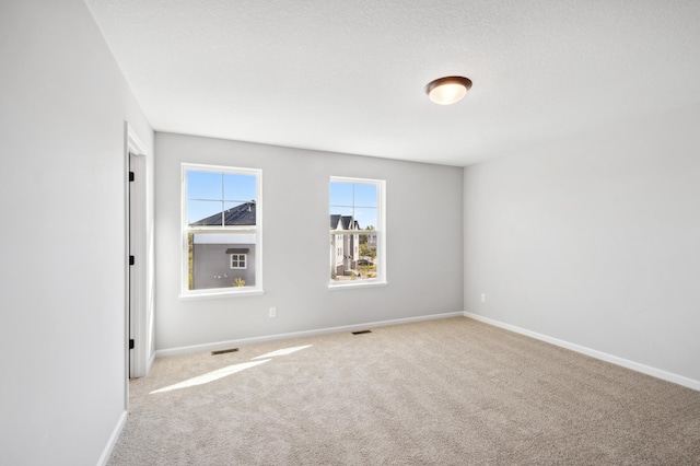 carpeted empty room featuring baseboards, visible vents, and a textured ceiling